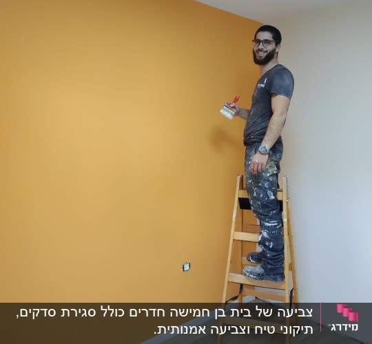 אדם צובע קיר בצבע כתום בעזרת מברשת.